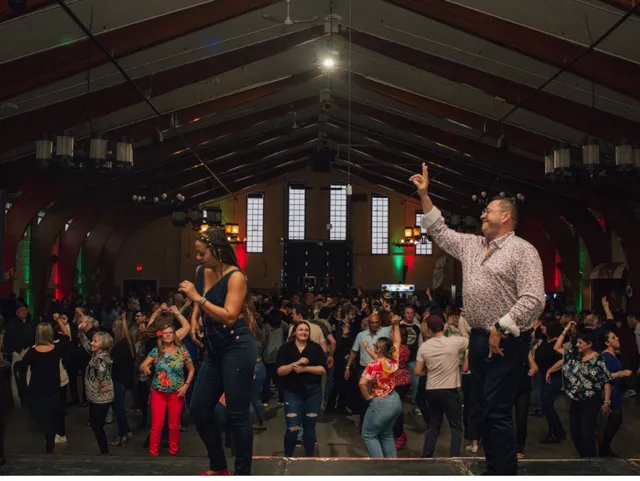 A packed Latin dance night in a large hall, with dancers on the floor and a host on stage